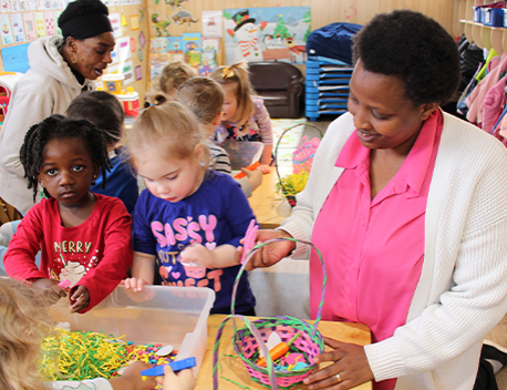 An instructor sits with students, helping them with an arts and crafts project